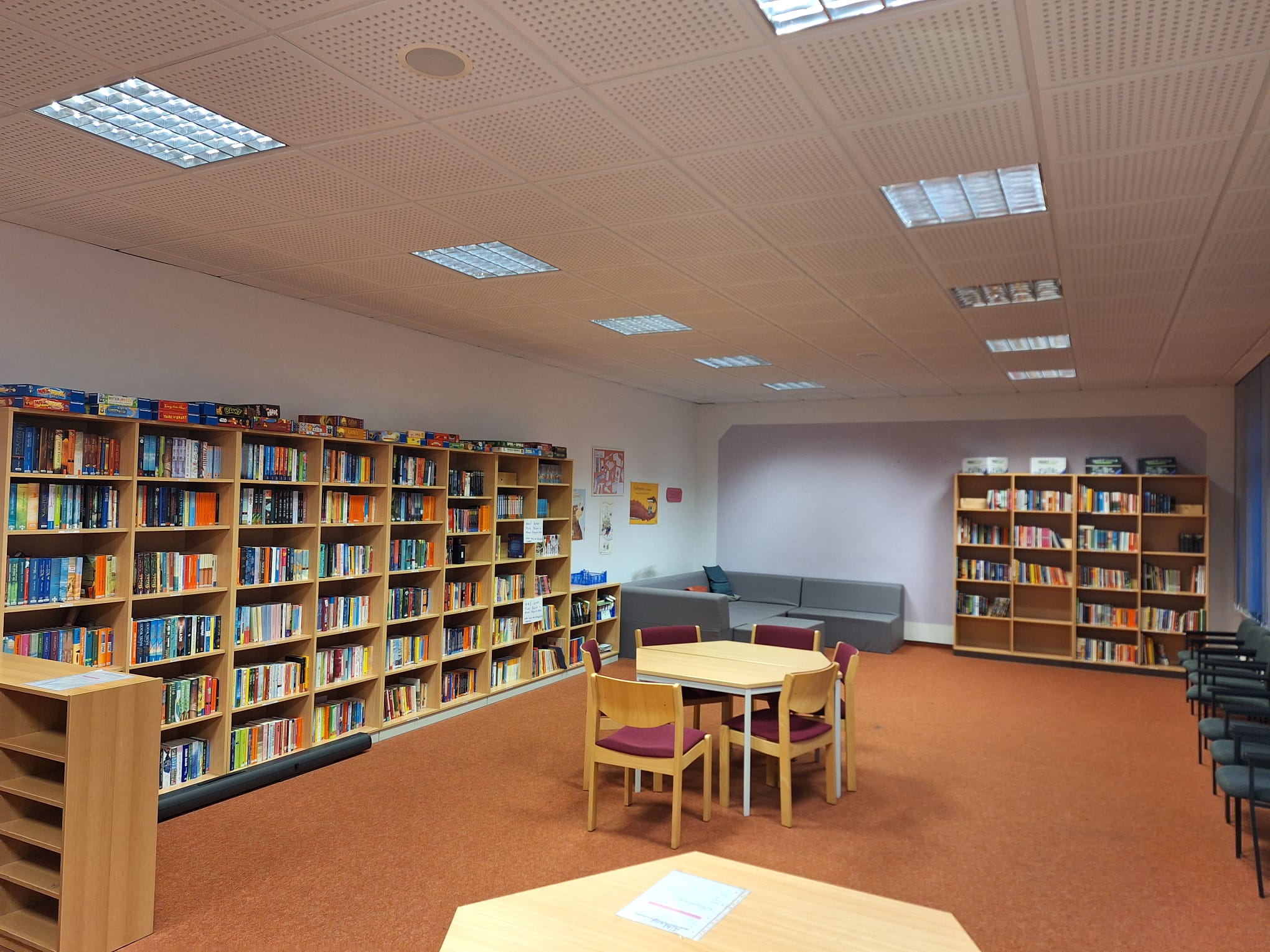 Innenansicht einer Bibliothek mit Regalen voller Bücher und Sitzgelegenheiten.