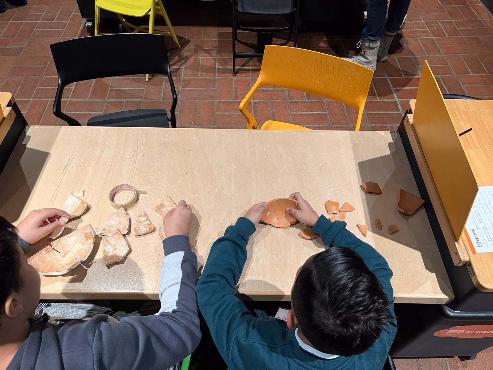 Kinder beim Wiederzusammenbauen eines Tongefäßes aus Scherben.