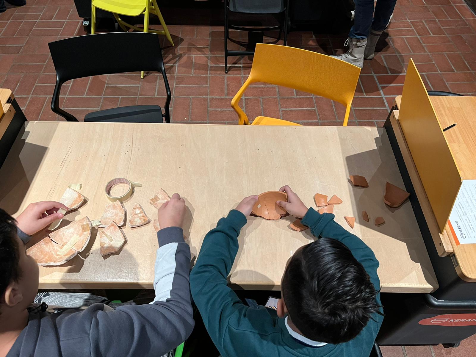 Kinder beim Wiederzusammenbauen eines Tongefäßes aus Scherben.