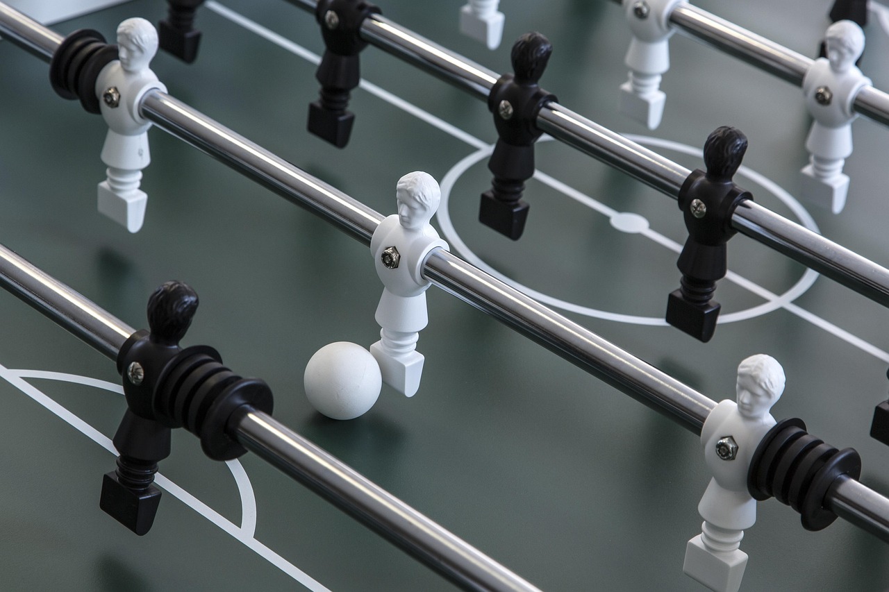 Aussschnitt aus einem Tischkicker mit schwarzen und weißen Figuren sowie einem Ball.