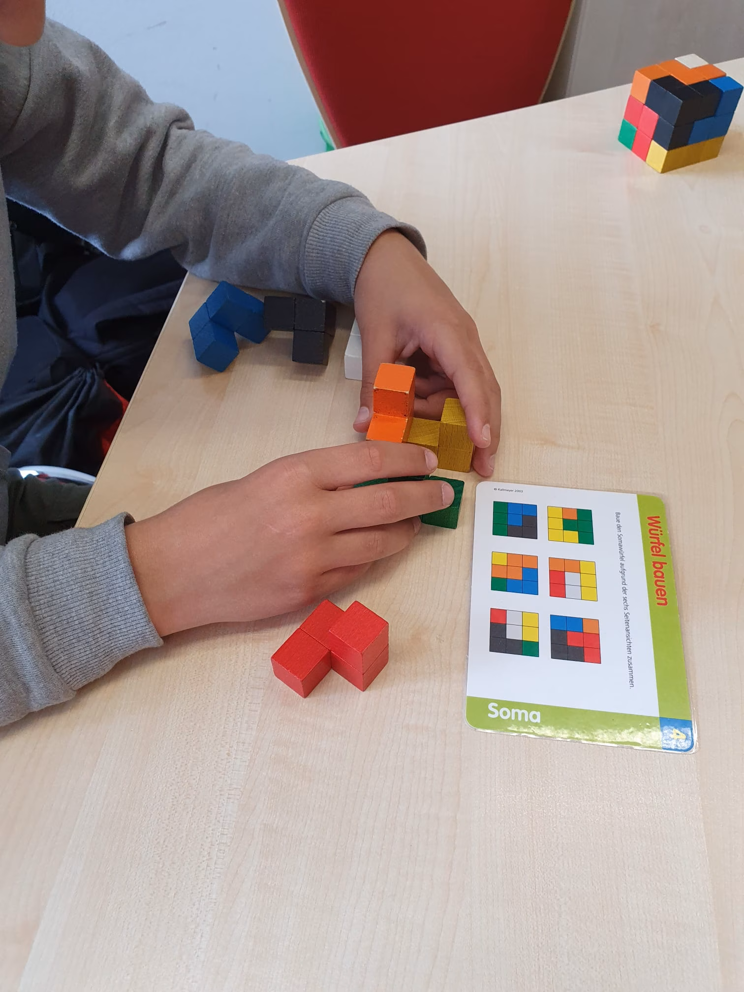 Ein Schüler baut nach Anleitung einen Würfel aus verschiedenen bunten Teilen zusammen.