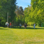 Ein Gruppe Schülerinnen und Schüler stehen auf einer Wiese und messen die Höhe eines Basketballkorbes.