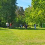 Ein Gruppe Schülerinnen und Schüler stehen auf einer Wiese und messen die Höhe eines Basketballkorbes.