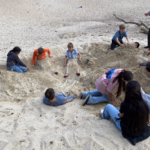 Eine Gruppe von Schülerinnen und Schülern liegt im Sand bzw. ist eingebudelt.