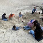 Eine Gruppe von Schülerinnen und Schülern liegt im Sand bzw. ist eingebudelt.