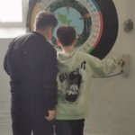 Zwei Schüler stehen vor einem Ausstellungstück. Dies ist rund mit viel Text.