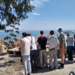 Eine Schülergruppe steht auf einem Berg und schaut von dort auf Malaga hinab. Es sind Häuser und das Meer zu sehen.