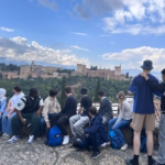 Eine Schülergruppe sitzt auf einer Mauer und schaut von dort auf die Alhambra hinüber.