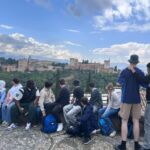 Eine Schülergruppe sitzt auf einer Mauer und schaut von dort auf die Alhambra hinüber.