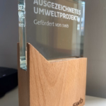 Pokal der unten aus Holz und oben auf Plastik besteht. Unten rechts in der Ecke steht swb. Im oberen Teil steht Ausgezeichnetes Umweltprojekt - gefördert von swb