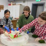 Drei Mädchen verteilen den grünen Kleber in einem weißen, runden Holzgestell.