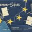 Eine blaue Fahne von Erasmus+ mit mehreren Blöcken, Kugelschreibern und Flaschen die auf der Flagge liegen.