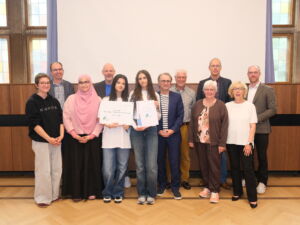 Schülerinnen mit einer Urkunde und dem Schild. Zudem einige Erwachsene