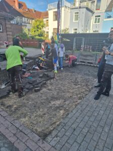 Gruppe von Kindern und Erwachsenen auf einer Baustelle mit aufgerissenem Boden