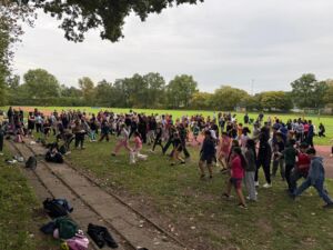 Große Gruppe von Kindern und Jugendlichen beim Aufwärmen auf einer Wiese neben einer Laufbahn bei bewölktem Himmel