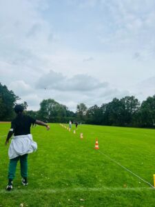 Person in Sportkleidung wirft einen Gegenstand auf einem großen Rasenfeld mit einer Reihe von orange-weißen Hütchen