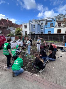 Gruppe von Menschen unterschiedlichen Alters arbeitet gemeinsam in einem städtischen Gartenbeetauf einem Schulhof